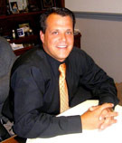Chris Rose, life & health agent, wearing a black shirt and orange tie at a wooden desk at V.R. Williams and Company in Winchester, TN