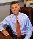Kevin Lockmiller, CIC at V.R. Williams and Company in Winchester, TN, wearing a blue shirt and orange tie at a wooden desk