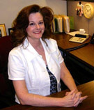 Lee Ann Gattis, CISR at V.R. Williams and Company in Winchester, TN. wearing a white button down over a black shirt at a brown desk